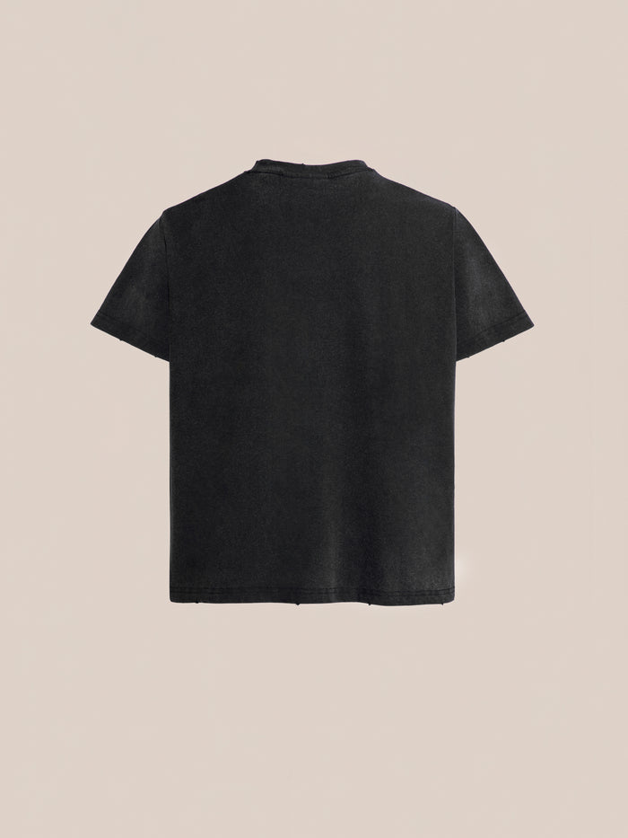 Back view of the Multi Patch Washed Tee, a plain black short-sleeve t-shirt from FOUND made from enzyme-washed cotton, set against a beige background.
