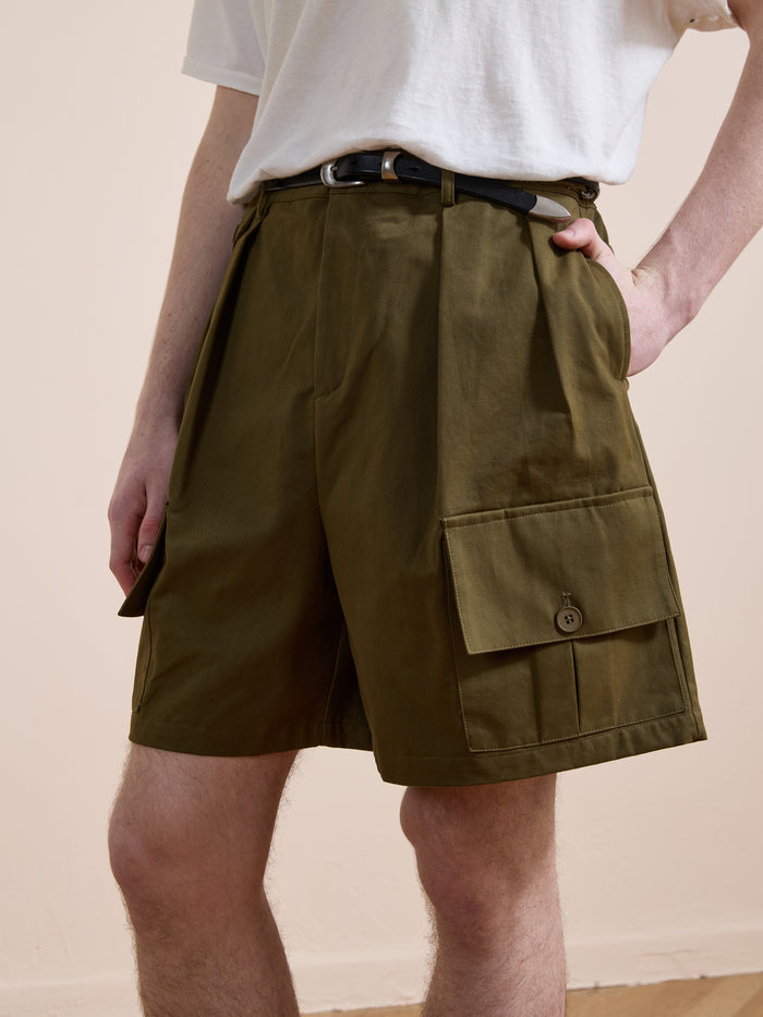 Someone wearing Found's Multi Pocket Shorts in olive green with a belt, paired with a white t-shirt, stands casually with one hand in their pocket against a plain background.