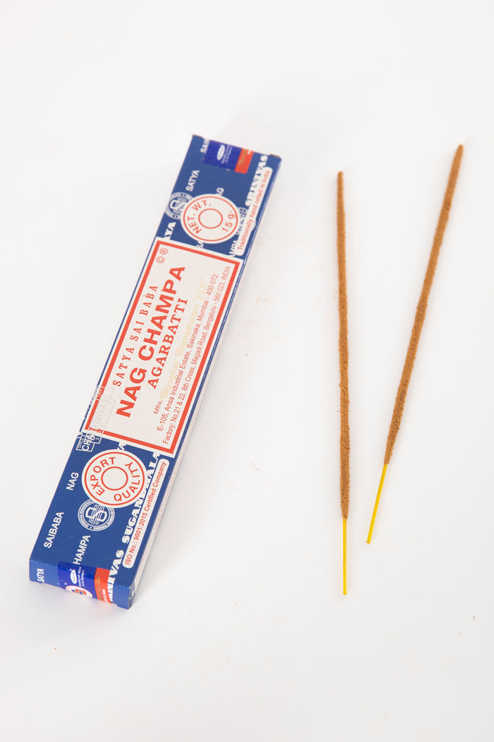 A box of Satya Sai Baba Nag Champa incense with two incense sticks placed in front of it on a white background.