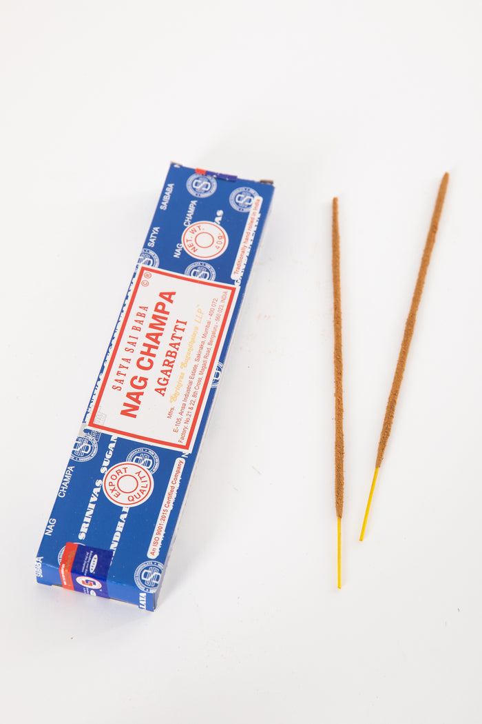 A box of Satya Sai Baba Nag Champa incense with two incense sticks placed in front of it on a white background.