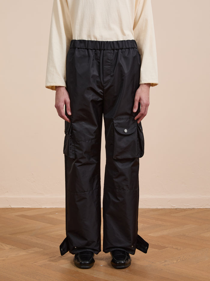 A person stands indoors on a wooden floor, wearing a cream long-sleeve top and FOUND Nylon Cargo Pants—a unisex, relaxed-fit style with large pockets.