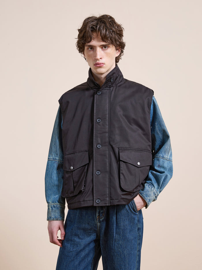 Someone wearing the FOUND Padded Cargo Vest in black over a blue denim jacket and blue jeans stands against a plain light background.
