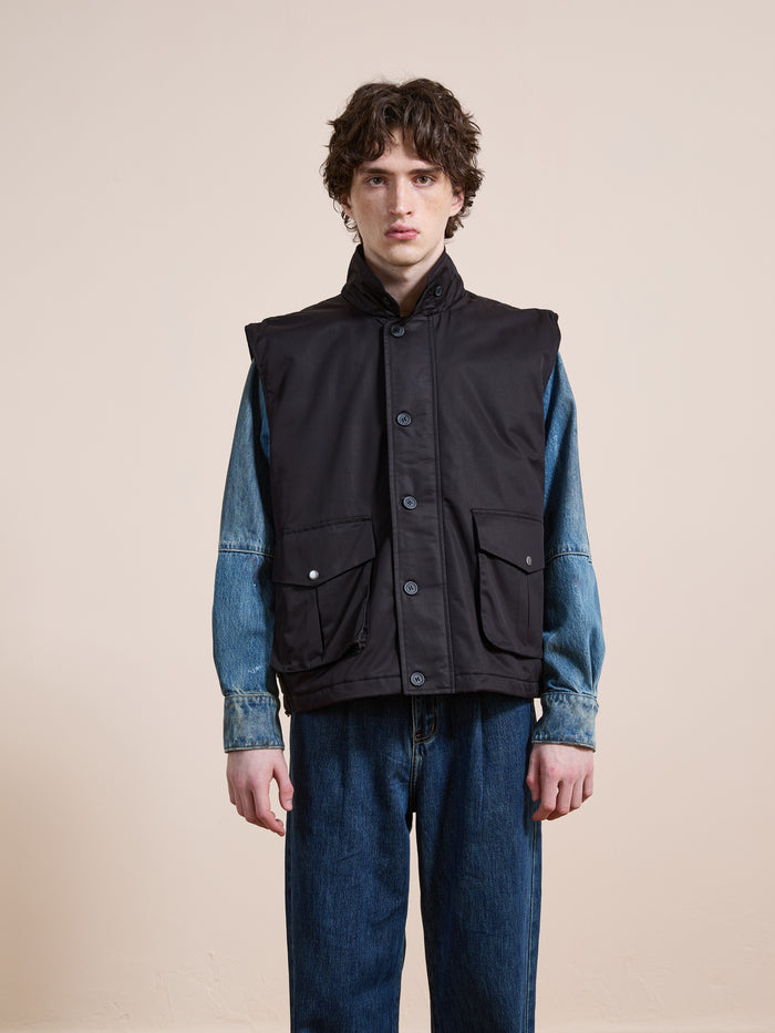 A person stands against a plain background wearing the FOUND Padded Cargo Vest over a denim jacket and blue jeans.
