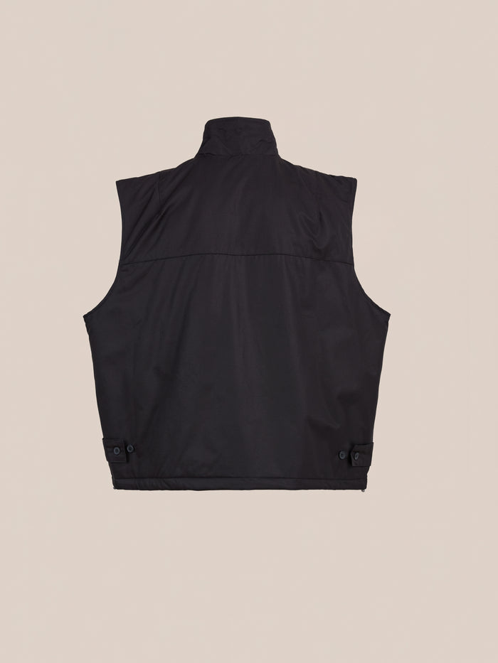 FOUND Padded Cargo Vest in black cotton twill shown from the back, with a high collar, straight hem, and adjustable button side tabs—ideal for layering. Displayed on a plain beige background.