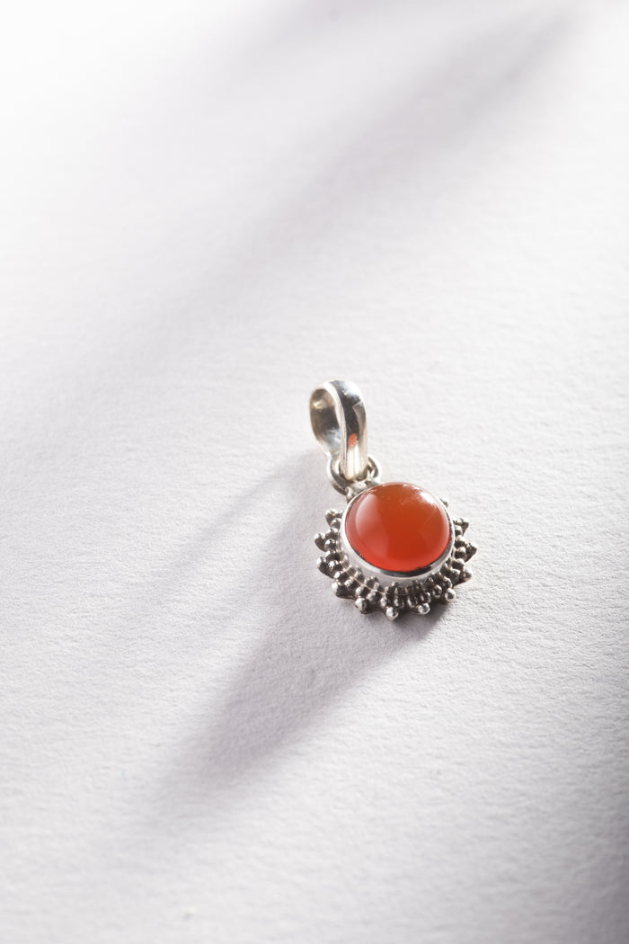 A round carnelian gemstone pendant set in a sterling silver floral design setting, photographed on a white background.
