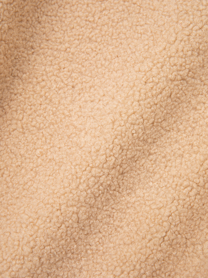 A detailed view of the Pahari Floral Embroidered Sherpa Pullover by FOUND, showcasing its beige fleece fabric with a textured, soft surface that evokes a sense of comfort.