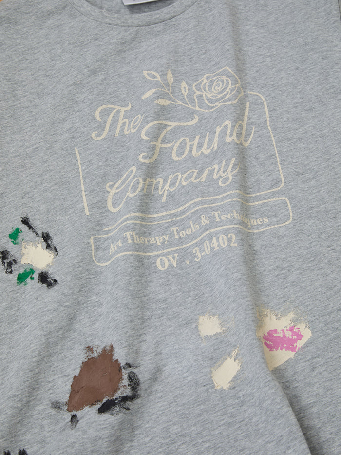 A gray unisex "Painters Company Tee" by FOUND showcases "Art Therapy Tools & Techniques," complemented by vintage-colored paint splatters on the lower part.