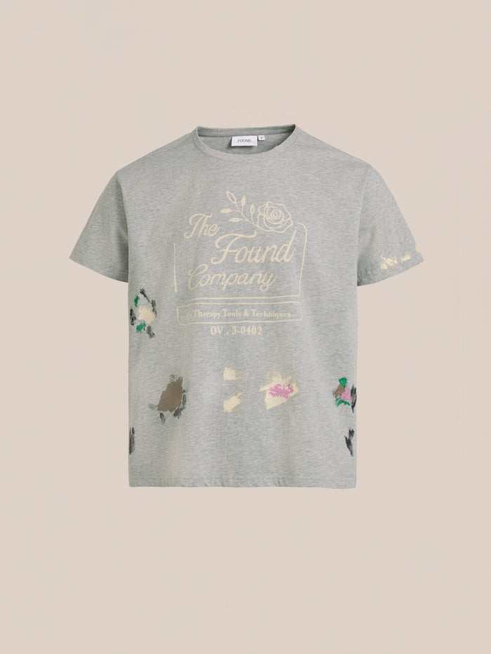 The FOUND Painters Company Tee is a gray vintage-style graphic t-shirt with "FOUND" text, a floral design, colorful paint splatters, and a unisex relaxed fit.