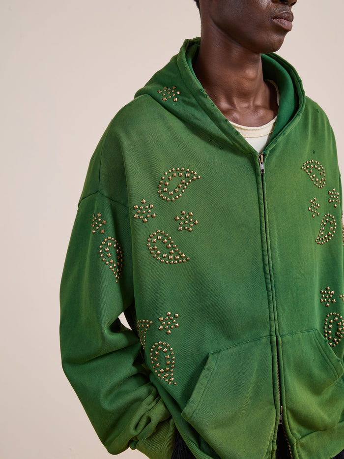 A person wears the FOUND Paisley Studded Zip Up Hoodie in green with star stud patterns over a white shirt, shown from the shoulders down—a vintage-inspired unisex style.