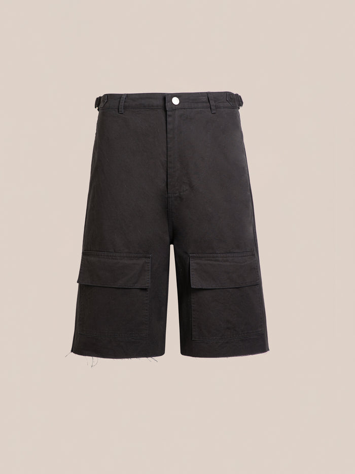 Found’s Parachute Cargo Twill Shorts—black, knee-length with large front flap pockets, button closure, belt loops, and frayed hem—offer utility style and are shown on a plain beige background.