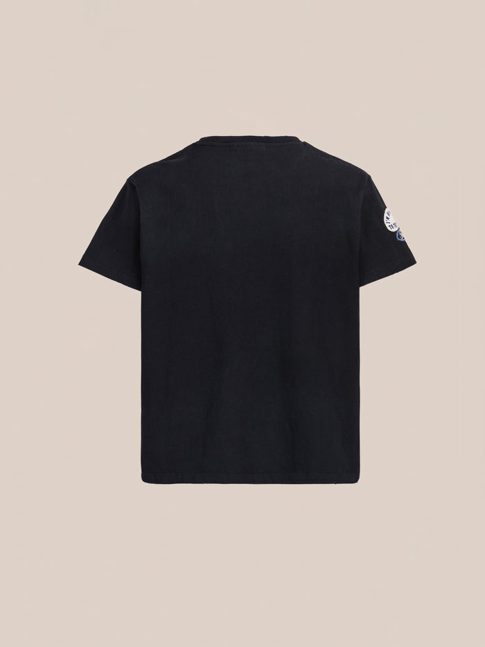 The FOUND Patchwork Camp Tee, a unisex relaxed fit in vintage black, is shown from the back against a light beige background.