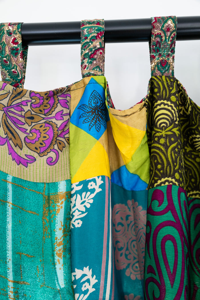 Colorful patterned green patchwork curtain hanging on a curtain rod against a white background