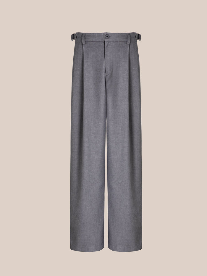 FOUND's Pleated Trousers feature a high-rise, gray wide-leg design with double pleats, button closure, and adjustable side tabs, all set against a simple beige backdrop.