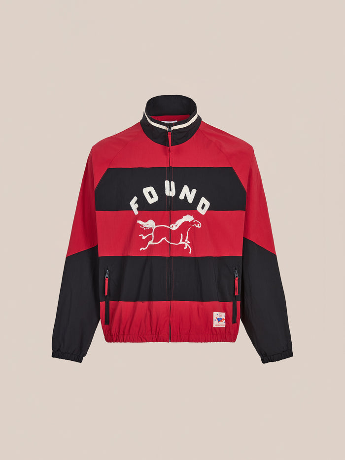 The FOUND Racing Striped Windbreaker is a red and black jacket with racing stripes, a horse graphic and "FOUND" on the front, two zippered pockets, and a small hem patch, inspired by vintage sportswear for a classic unisex look.