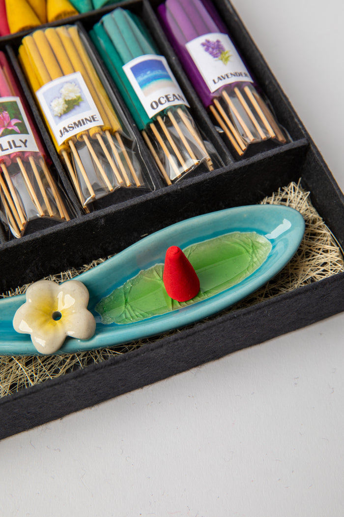 Leaf-shaped ceramic incense holder with flower detail and red incense cone ready for burning