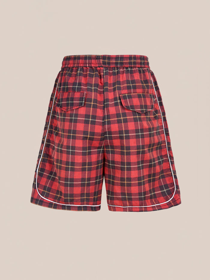 Found Red Plaid Track Shorts feature black and red plaid design with white piping, elastic waistband, two back pockets, and a unisex relaxed fit for a vintage athletic look—all shown against a plain beige background.