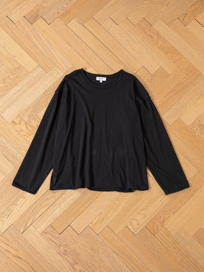 The FOUND Reversed LS Tee in plain black, made from premium materials, is displayed flat on a light wood herringbone floor.