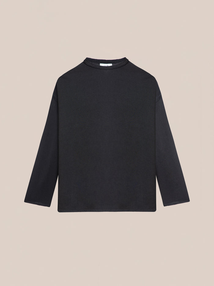 The FOUND Reversed LS Tee in plain black, featuring a relaxed fit and crew neckline, is displayed against a beige background.
