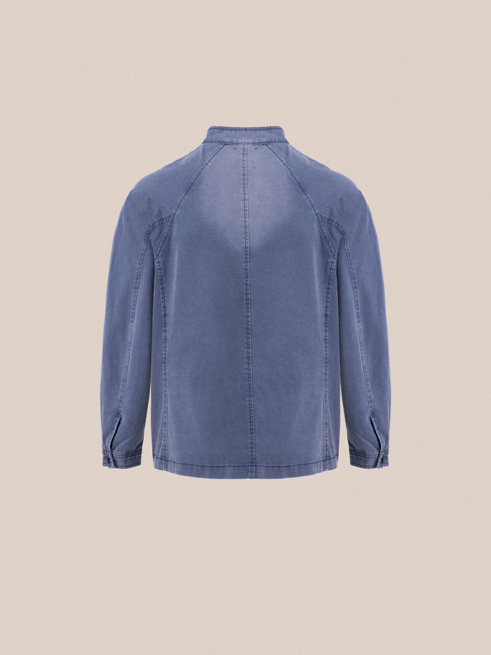 The back view of a blue Found River Painters Chore Coat on a beige background.