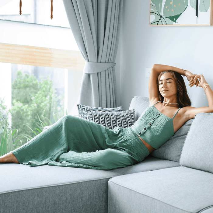 Model sitting on couch wearing a sage cotton tank top and sage wide leg cotton pants
