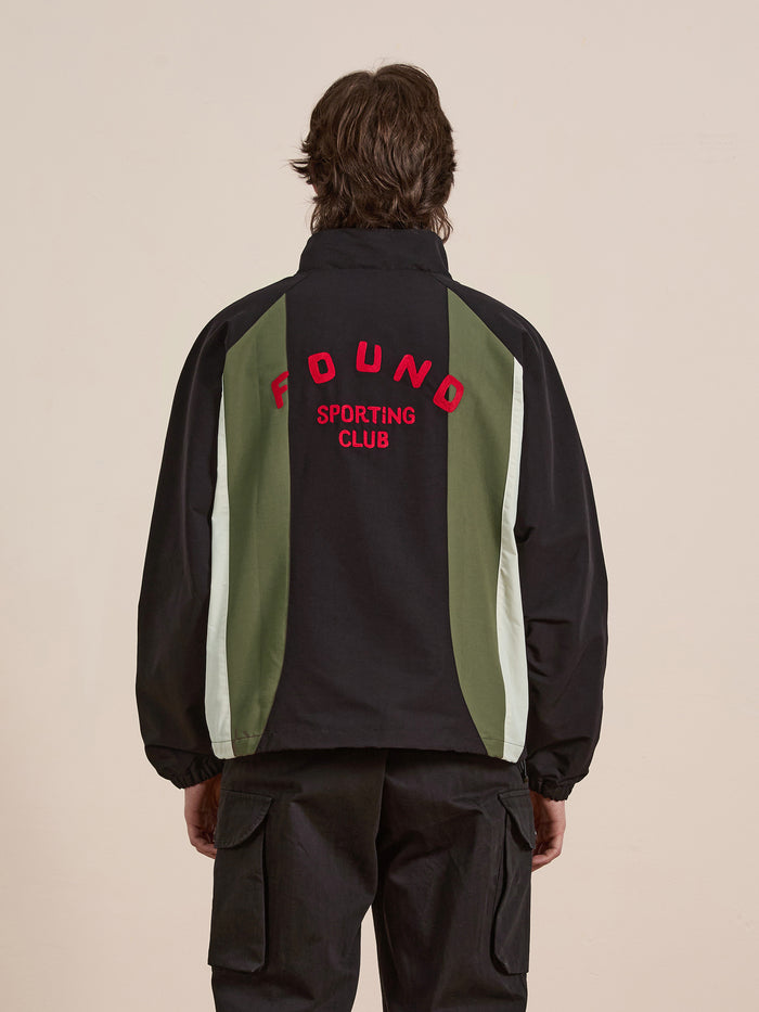 A person is wearing the FOUND Sporting Club Pullover Jacket, which has "FOUND SPORTING CLUB" on the back and black, green, and white panels for a vintage look.