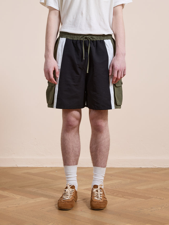 A person wearing a white t-shirt, Found Sporting Club Track Shorts with green pockets, white socks, and brown sneakers stands on a wooden floor against a plain wall.