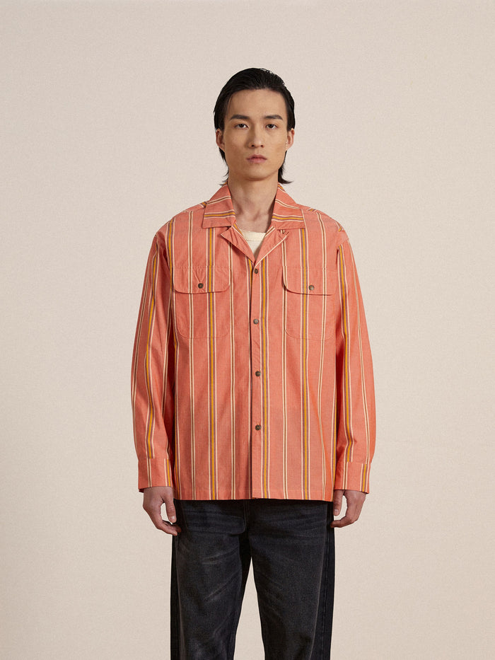 A man wearing an orange Found Stripe Citrus LS Camp Shirt and jeans.