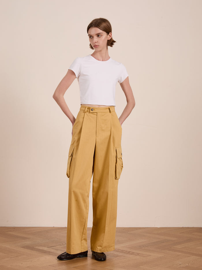 A person in a white t-shirt and FOUND's Sunlight Twill Cargo Pants stands with hands in pockets on a wooden floor against a plain background.
