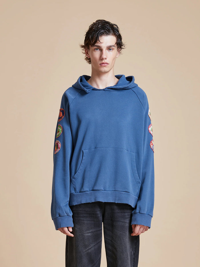 A man wearing a Found Timber Campground Hoodie, featuring vintage-inspired campground patches, and black pants.