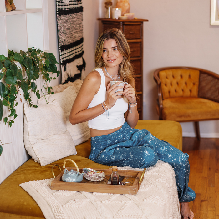 Turquoise Cosmic Sky Harem Pants, seated with a mug