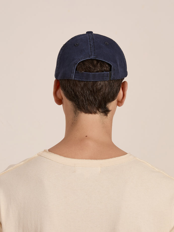 Back view of a person wearing the FOUND Two-Tone Logo Cap in deep navy with a distressed red brim, paired with a beige shirt.