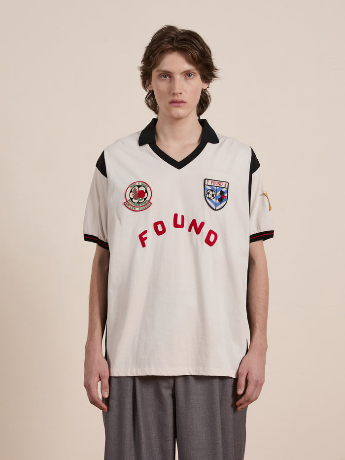 Clad in a sleek Union Soccer Jersey by FOUND, featuring bold "FOUND" text and badges, an individual stands against a plain backdrop, reminiscent of contemporary sportswear design.
