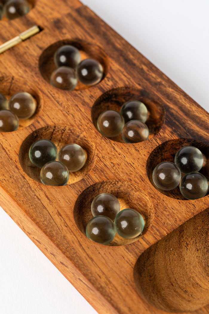 Glass marbles resting in carved wooden mancala pockets — artisan wooden game for kids and families.