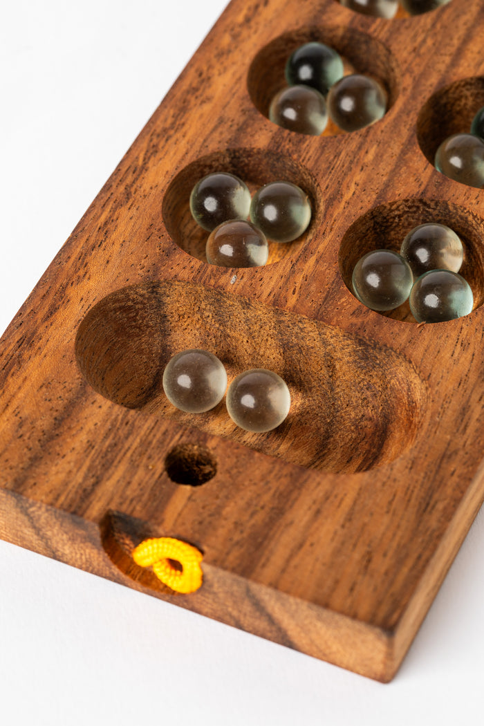 Glass marbles resting in carved wooden mancala pockets — artisan wooden game for kids and families.