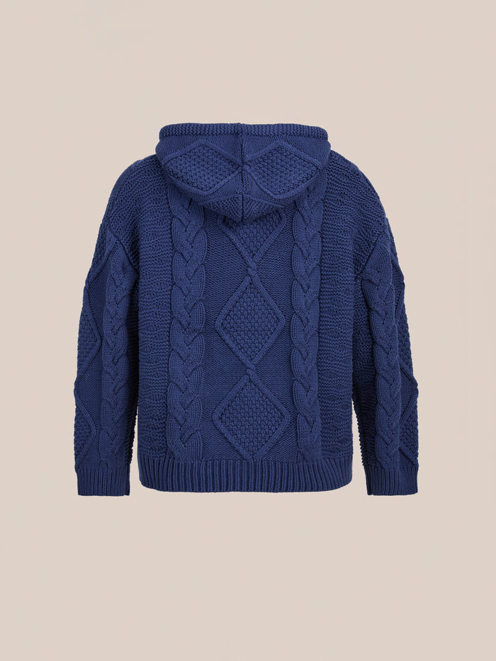 The Found Zip Up Cable Knit Hoodie, shown from the back on a beige background, features diamond and braided patterns. This unisex sweater blends classic cable texture with modern comfort and style.